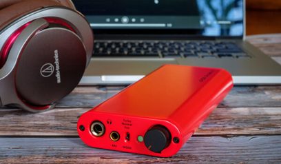 Bærbar iFi Audio iDSD Diablo rød lydkonverter, set forfra, ved siden af et sort og sølv hovedsæt på et træbord