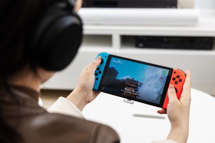 Console Nintendo Switch portatile blu e rosso in uso, tenuta a due mani, vista da dietro con cuffie audio