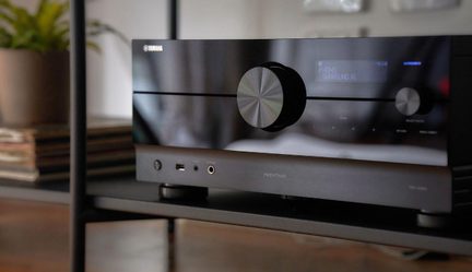 Yamaha Aventage domáci kinoamplifér v čiernej farbe s lesklým čelným panelom, veľkým centrálnym ovládačom a modrým digitálnym displejom na TV stolíku