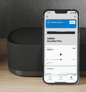 Sort Sennheiser AMBEO Soundbar Plus og mobilapplikation til konfiguration på hvid smartphone-skærm