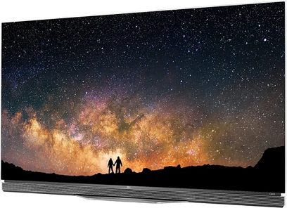 Stjernebestrøet himmel med Mælkevejen og silhuetter af to personer i forgrunden mod en baggrund af bjerge