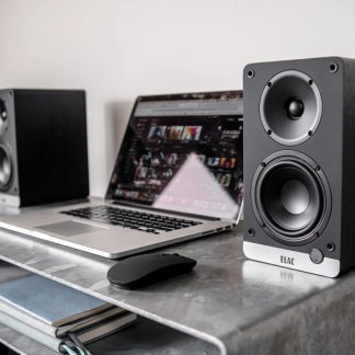 Aluminium-Laptop und Paar schwarzer Holzlautsprecher mit Hochtönern und Tieftönern auf dem Schreibtisch, Dreiviertelansicht