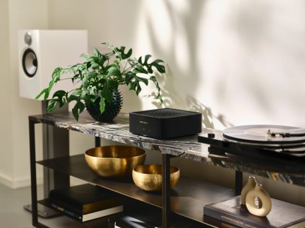 Hvit høyttaler, grønn plante, gylden bolle, gylden bolle, bok, bok, beige vase, platespiller, møbel i tre og metall