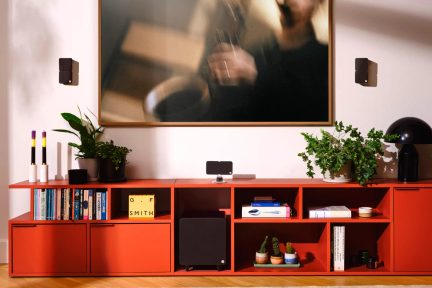 Sort lydsystem med væghængte højttalere, centerhøjttaler og subwoofer på rødt møbel