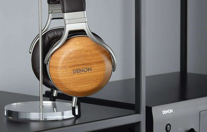 Denon AH-D9200 hovedtelefoner i naturtræ, set fra venstre profil, placeret på en metalstøtte, med "DENON"-logo på ørekoppen