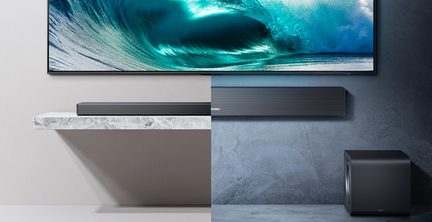 Černý matný soundbar s drážkovaným předním mřížkováním, pohled zepředu, doplněný černým matným krychlovým subwooferem s bočním kovovým basreflexem