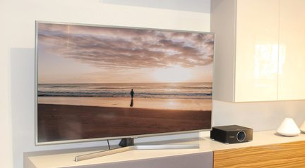 Fjernsyn der viser en strand ved solnedgang, med en menneskelig silhuet i det fjerne på sandet nær havet