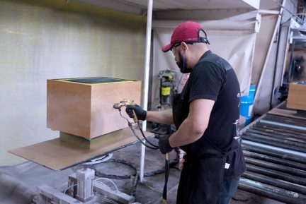 Craftsman applying a spray finish to a wooden cabinet in a paint workshop