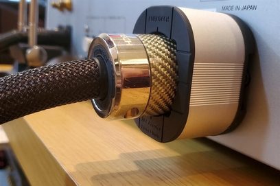 Furutech NCF Booster Brace Single i metal og kulstof, tæt sidevinkelbillede på en lys træoverflade