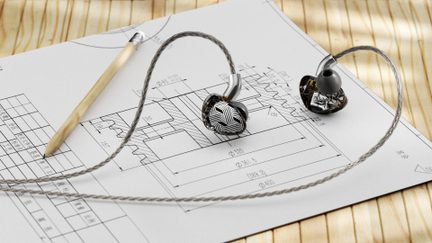Auriculares intrauditivos con cable, de plástico negro translúcido, con un diseño geométrico blanco en una carcasa, almohadillas grises y cable trenzado plateado, vista superior