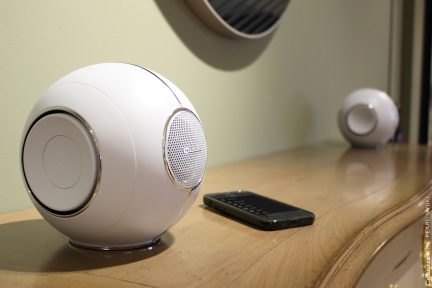 Dvě bílé kulové reproduktory a černý smartphone položené na dřevěném povrchu, pohled v perspektivě