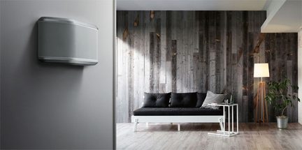 Black sofa on a wooden floor in a room with dark wood walls, a gray wall lamp, and a green plant in a white pot