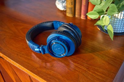 Sluchátka Audio Technica ATH-M50xBT2DS modro-černá, z boku, položená na dřevěném stole s zelenou rostlinou v pozadí