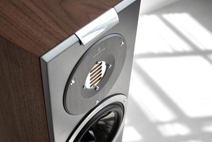 Brun træ hi-fi-højttaler med antracitgrå metalfront, diskant med rillet gitter og sort woofer omkranset af skruer, set i trekvart fugleperspektiv