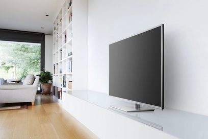 Sort fladskærms-tv stående på et hvidt møbel i et moderne indendørsmiljø med et stort hvidt bogreoler