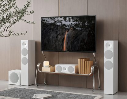 Stue, set forfra, sort TV med glasplade, hvide højttalere med grå stofgitter, centerhøjttaler og subwoofer, metalmøbel