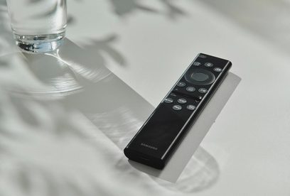 Sort Samsung fjernbetjening på hvid reflekterende overflade tæt på et glas vand, set fra oven