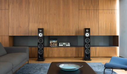 Paar zwarte hi-fi vloerstaande luidsprekers in een moderne woonkamer met houten wandmeubel, vooraanzicht