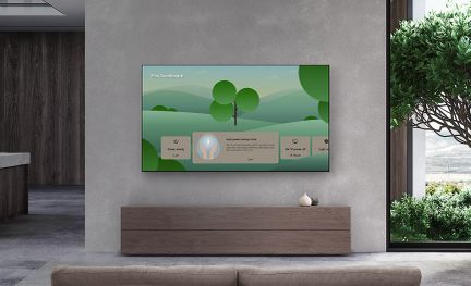 Platte wandtelevisie met een groen dashboard, lage houten kast, witte vaas, grijze muur, raam rechts, boom buiten