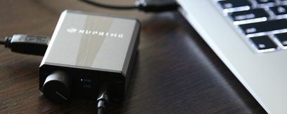 Nuprime uDSD sort, bærbar audio-konverter, set ovenfra, liggende på et sølvfarvet computertastatur