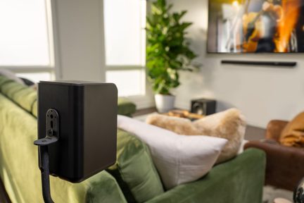 Schwarze Standlautsprecher aus der 3/4-Rückansicht in einem Wohnzimmer, grünes Sofa und grüne Pflanze im Hintergrund