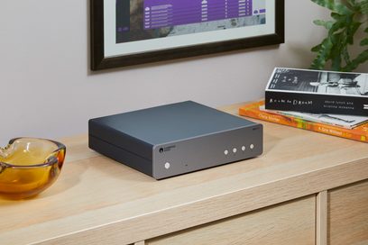 Cambridge Audio MXN10 nettverksmottaker i sølv, forfra, plassert på en lys trehylle, ved siden av bøker og en ambrafarge bolle
