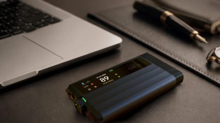 Amplificatore per cuffie DAC portatile nero con display digitale e manopola del volume, posizionato accanto a un computer portatile