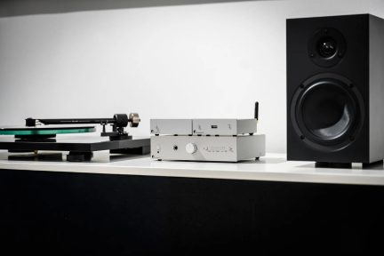 Сребриста hi-fi система Pro-Ject с грамофон и черна тонколона върху бяла мебел